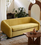 A modern curved yellow fabric sofa in a styled living room setting with a wooden coffee table.