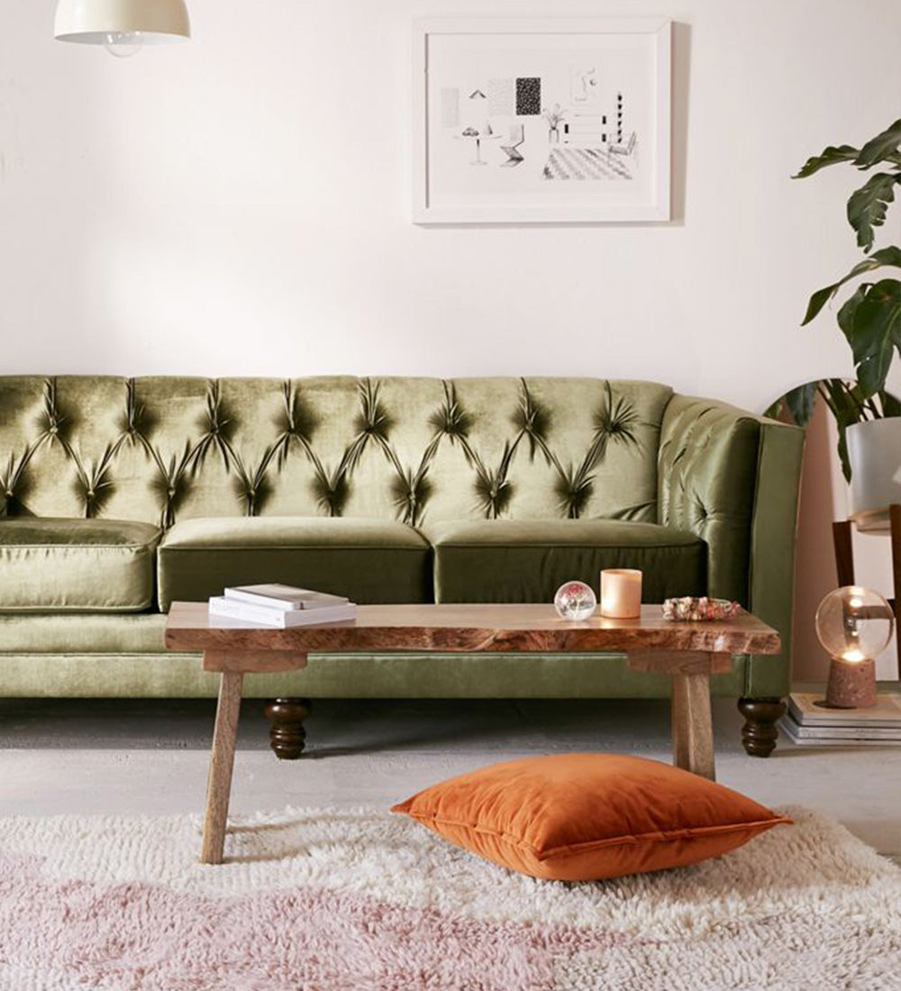 An olive green tufted velvet sofa in a styled living room setting