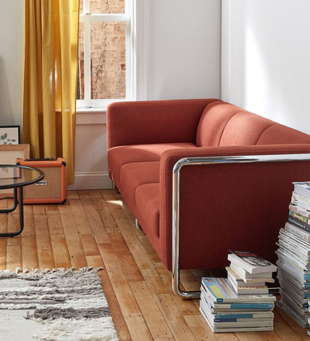 A rust-orange upholstered corner sofa with a chrome metal frame sits in a bright living room